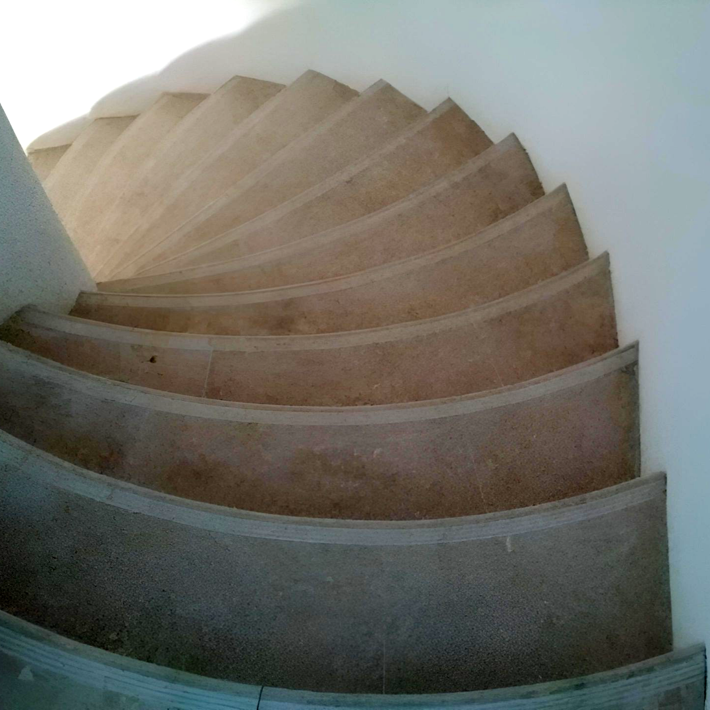 Vue en plongée d'un escalier en colimaçon étroit et incurvé en béton, aux marches simples de couleur neutre.