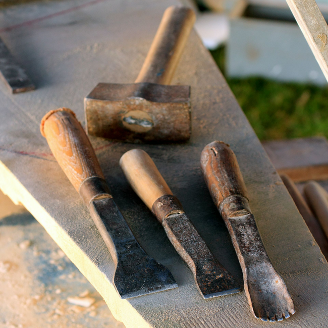 Un maillet en bois et trois ciseaux à bois en métal à manches en bois reposent sur une surface de travail grise et texturée.