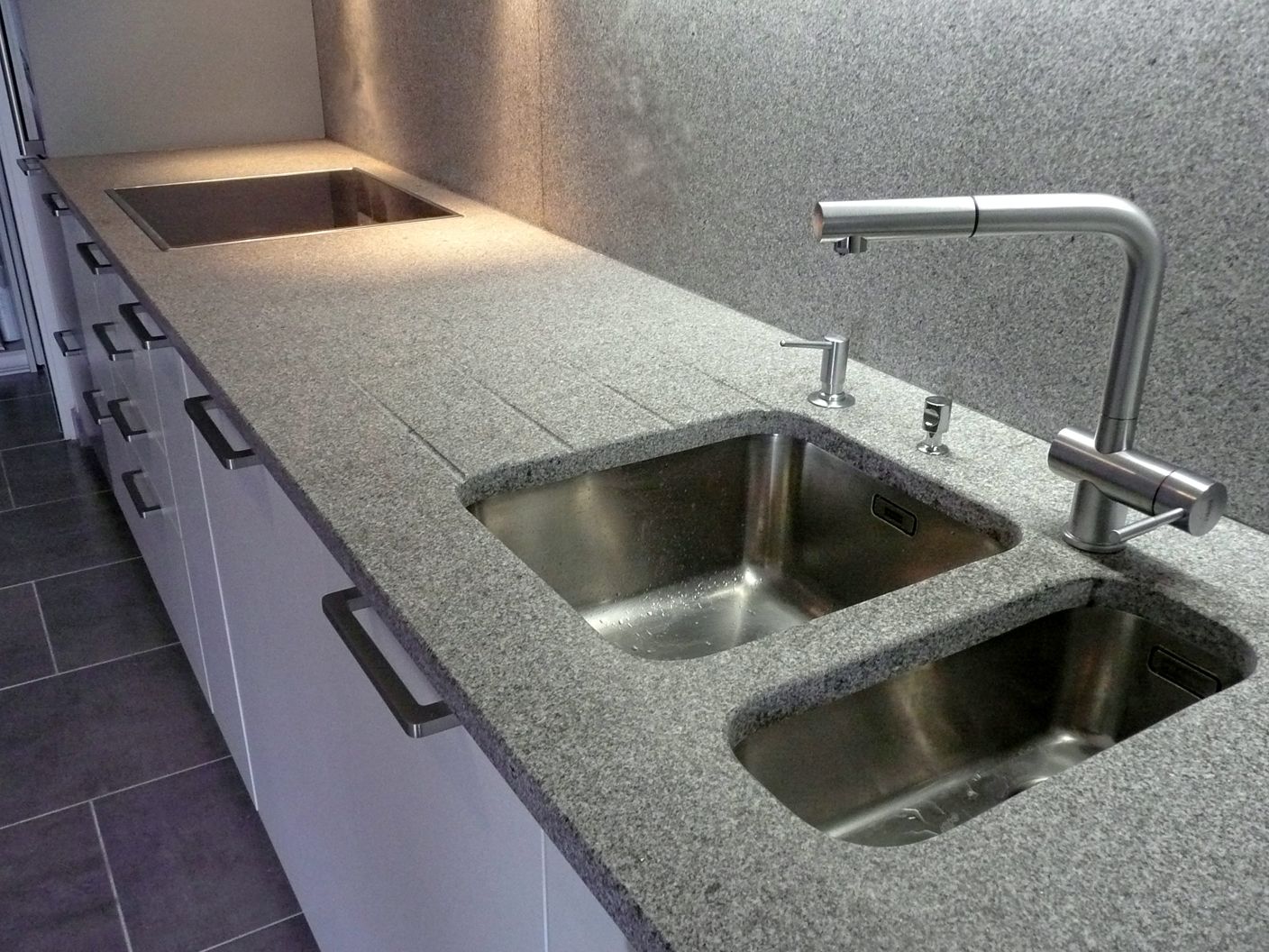 Un plan de travail de cuisine moderne avec une surface en granit gris moucheté, un évier double en acier inoxydable et un robinet assorti.