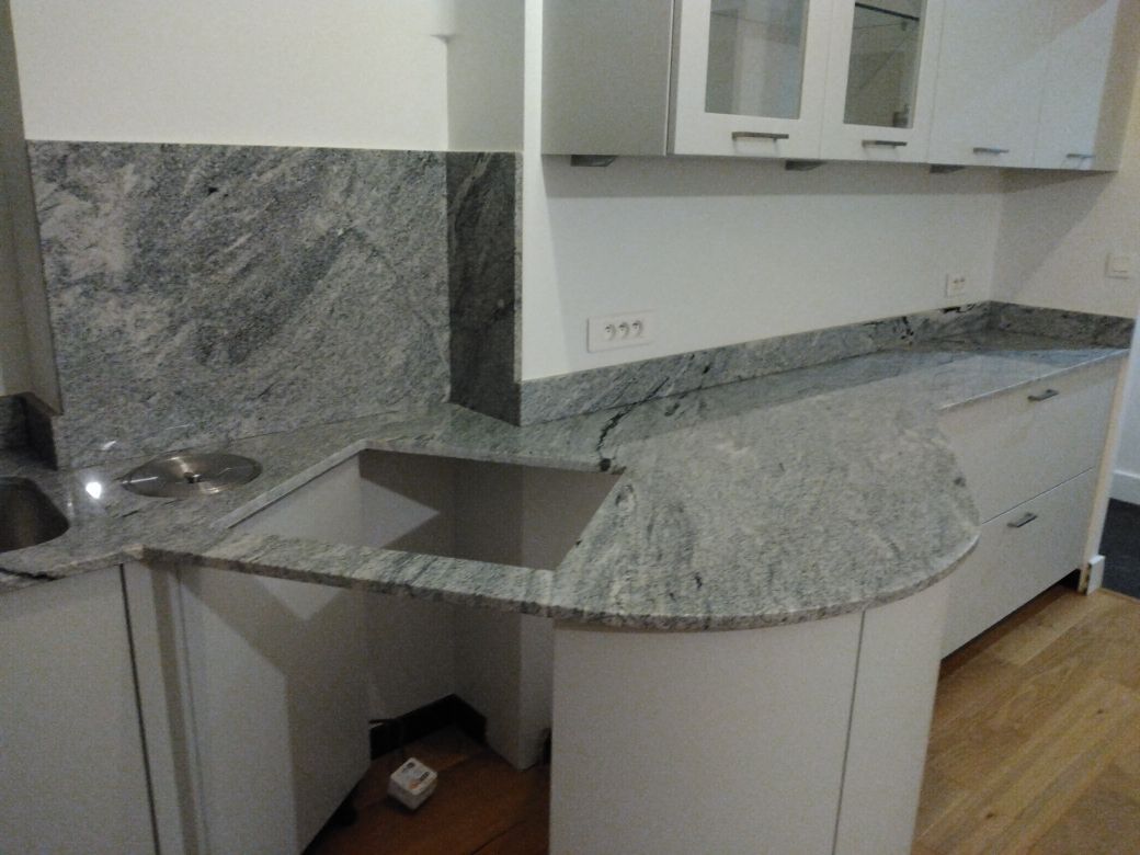 Une personne vêtue de vêtements couverts de poussière utilise un maillet et un burin pour tailler un gros bloc de marbre blanc.