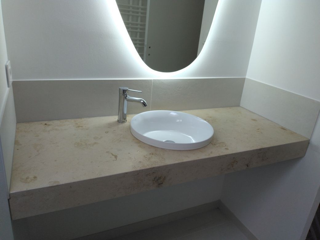 Petit meuble-lavabo de salle de bain avec lavabo rond blanc, robinet chromé et miroir rétroéclairé au-dessus d'un plan de travail beige.