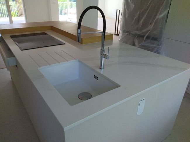 Îlot de cuisine moderne avec évier blanc, robinet noir et plaque de cuisson intégrée près d'une fenêtre