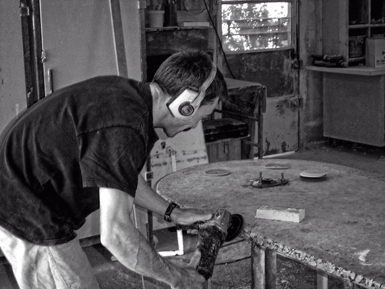 Dans un atelier, une personne portant un casque de protection utilise une meuleuse d'angle pour poncer le bord d'une table ronde en bois.