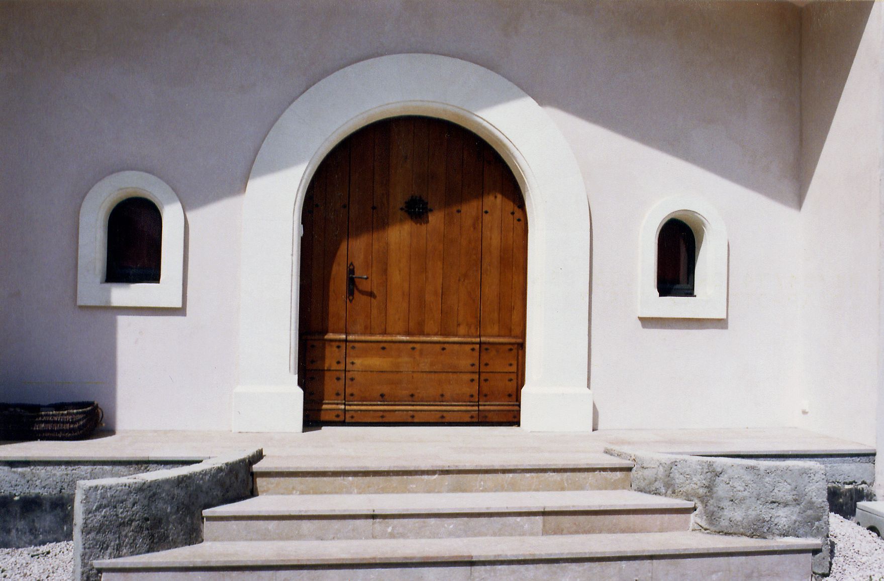 Entrée d'église blanche avec porte cintrée en bois et marches en pierre y menant