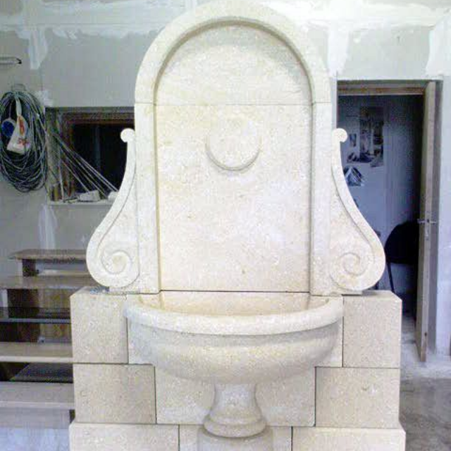 Sculpture de lavabo en pierre blanche contre un mur carrelé dans un atelier ou une salle de bains en construction