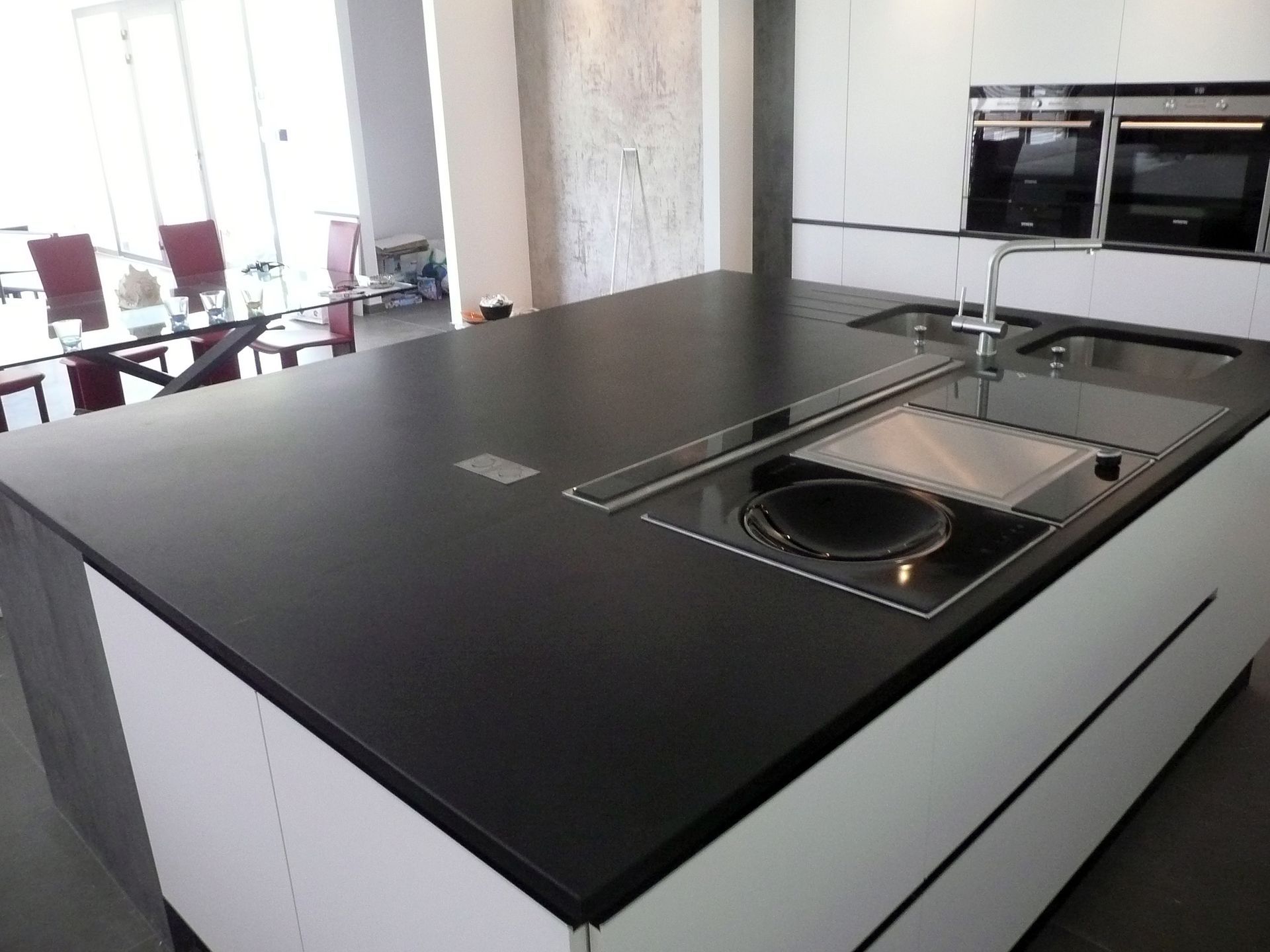 Îlot de cuisine moderne avec comptoir noir, évier intégré et plaque de cuisson dans une pièce lumineuse à aire ouverte