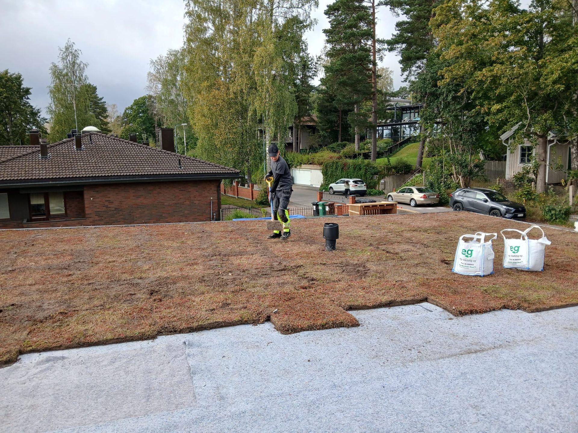 Takapiha, jossa on puuhaketta, työntekijä, puita ja pihatarvikkeita tiilitalon vieressä