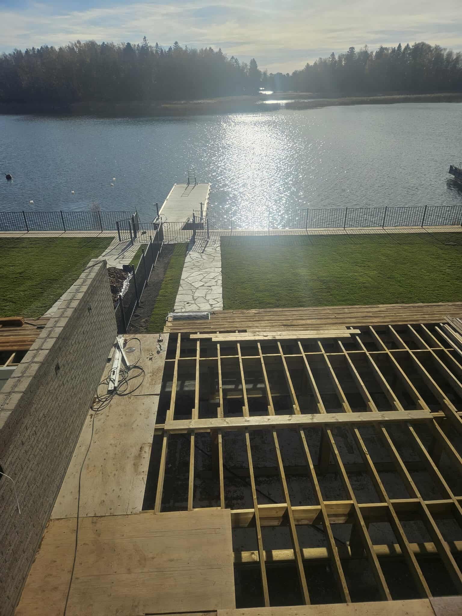 Aurinkoinen järvinäkymä rakenteilla olevalta terassilta. Etualalla näkyy puurunkoinen rakennelma ja ulapalle ulottuva laituri