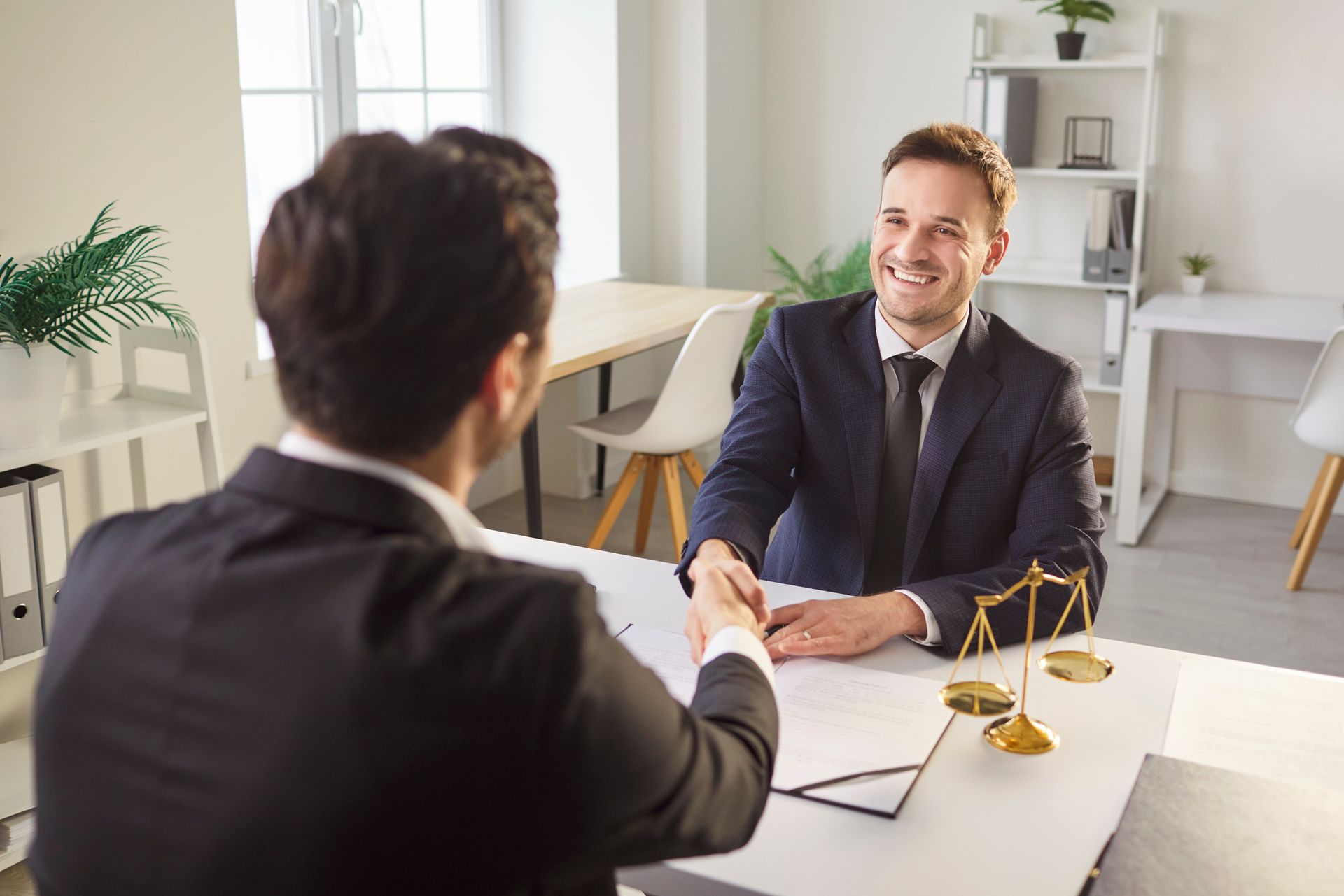 Deux hommes en costume se serrent la main par-dessus un bureau, dans un environnement de bureau. L'un d'eux sourit.
