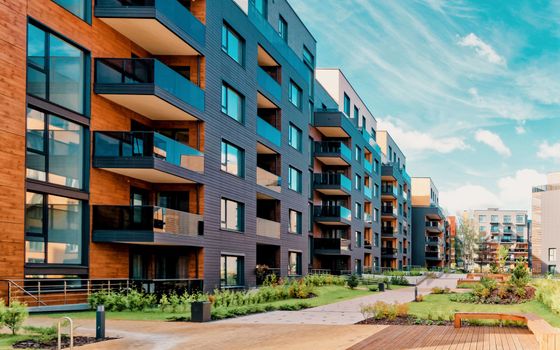 Immeubles d'appartements modernes avec balcons, façades en briques sombres, espaces verts et ciel bleu.