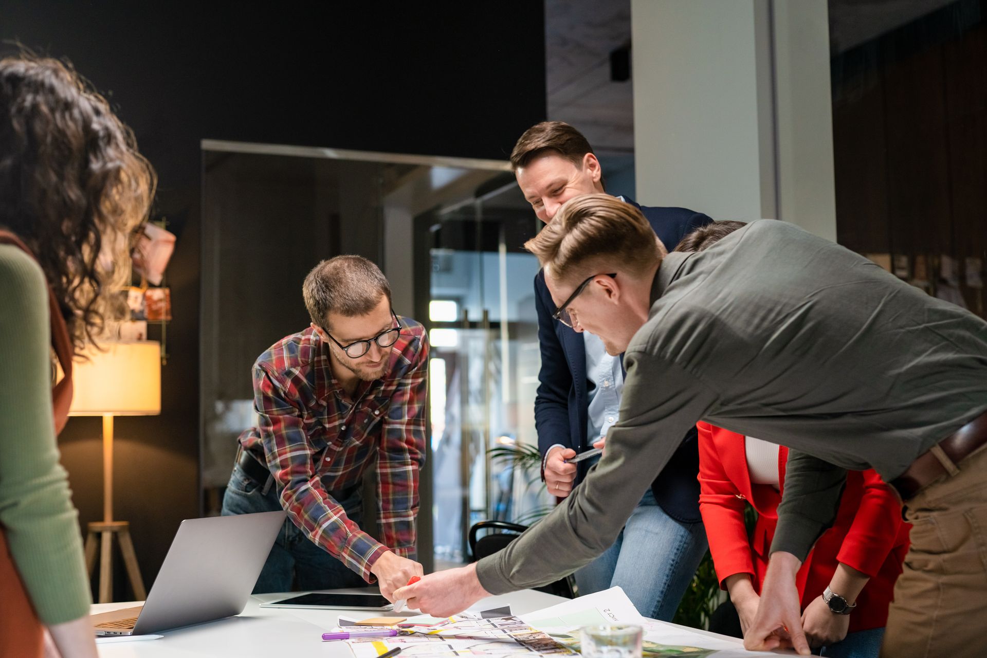 Un groupe de personnes collaborant autour d'une table avec un ordinateur portable, des papiers et des câbles en train de faire un brainstorming dans un bureau.