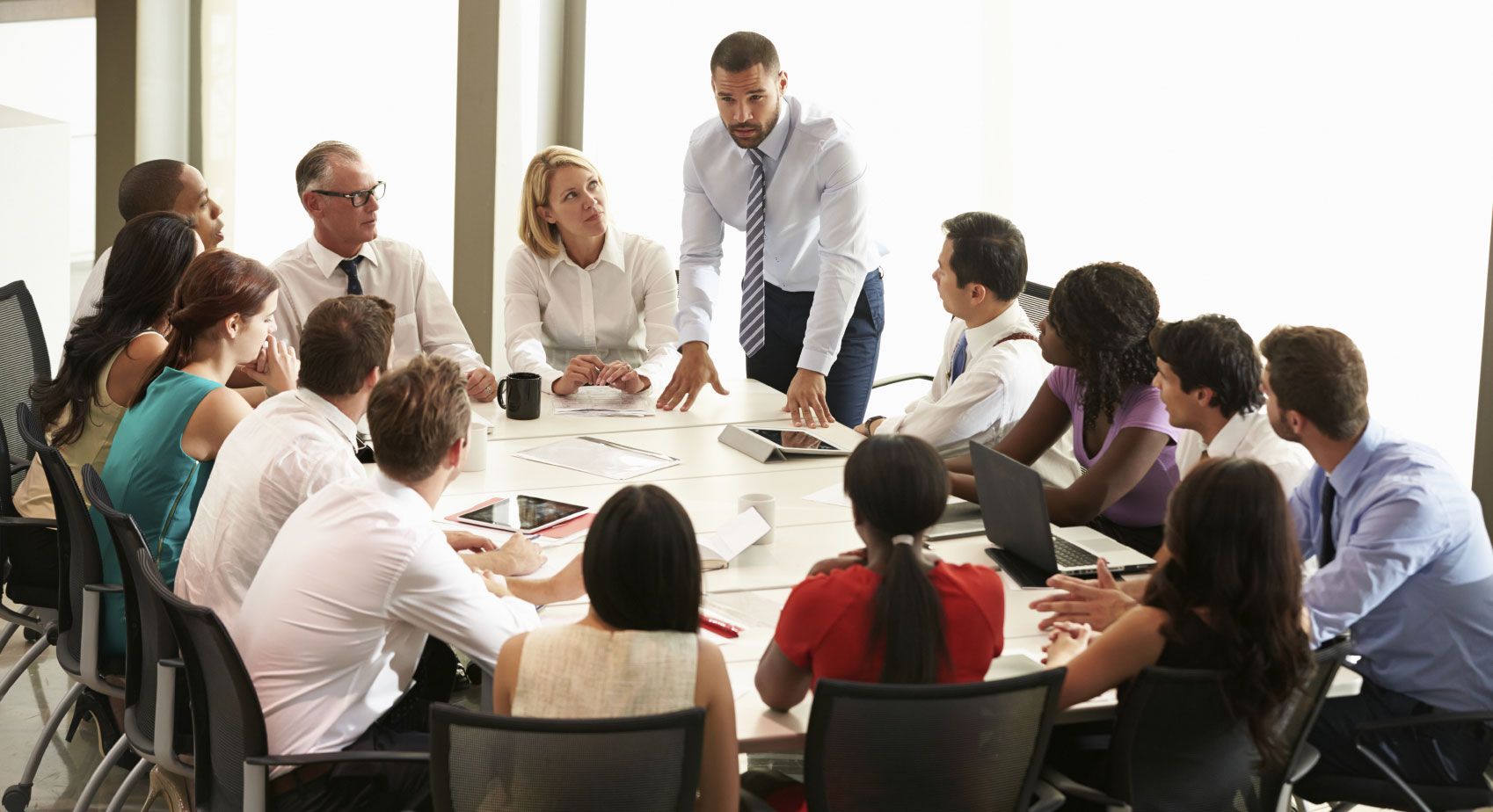 Réunion d'affaires autour d'une grande table ; collègues discutant d'idées et de documents dans un bureau.
