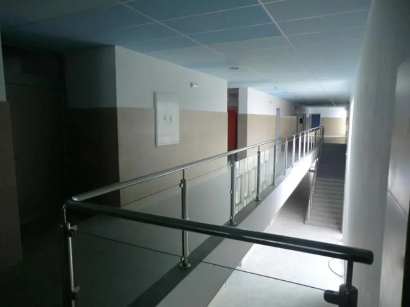 Un largo pasillo con barandilla de cristal y escaleras.