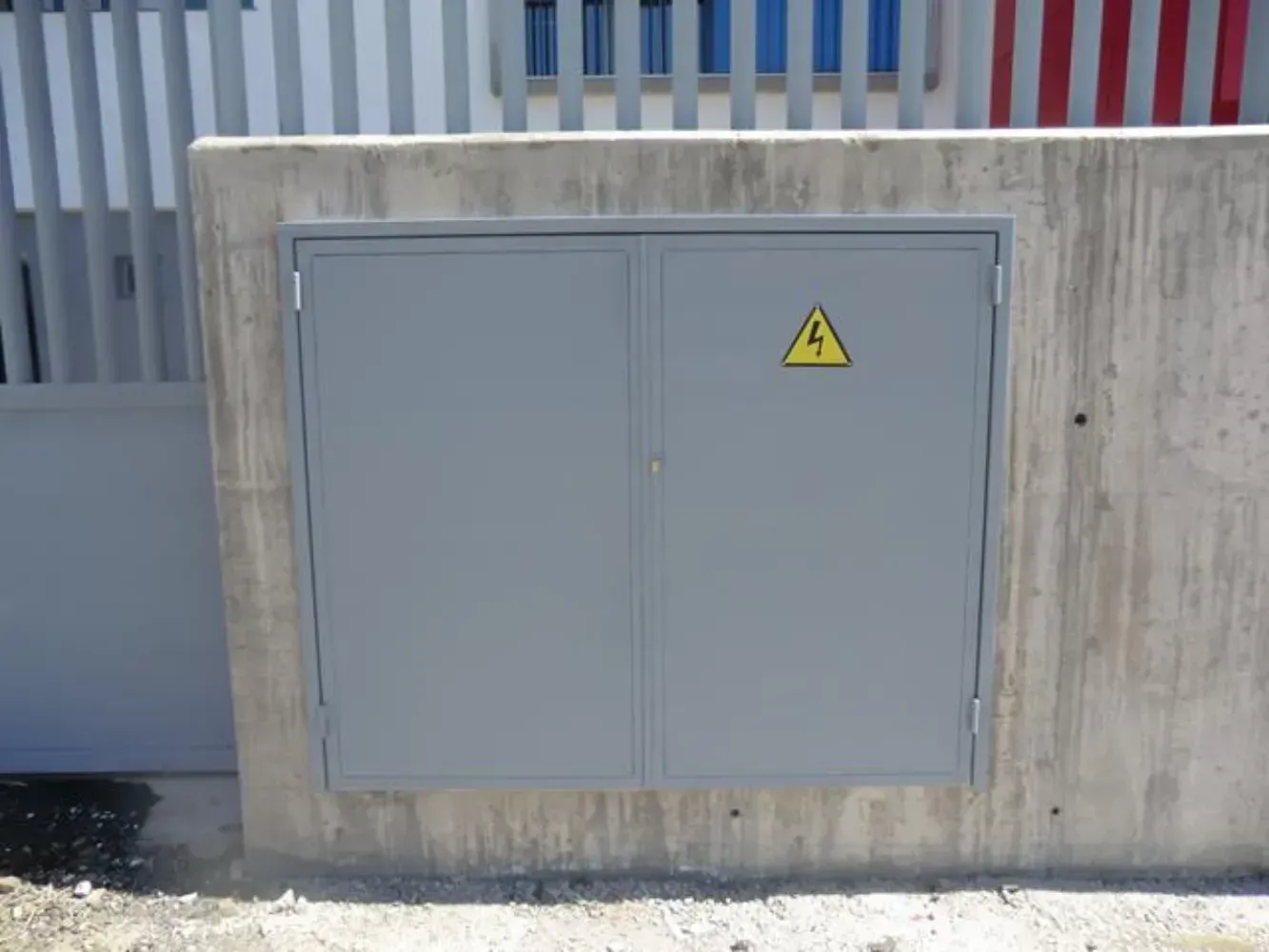 Un muro de hormigón con una puerta metálica y una señal de advertencia amarilla sobre él.