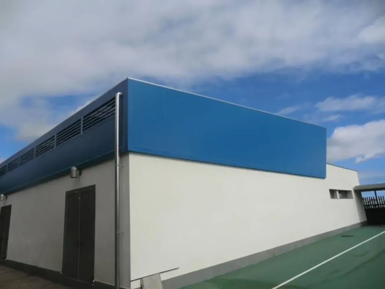 Un edificio azul y blanco con una cancha de tenis enfrente.