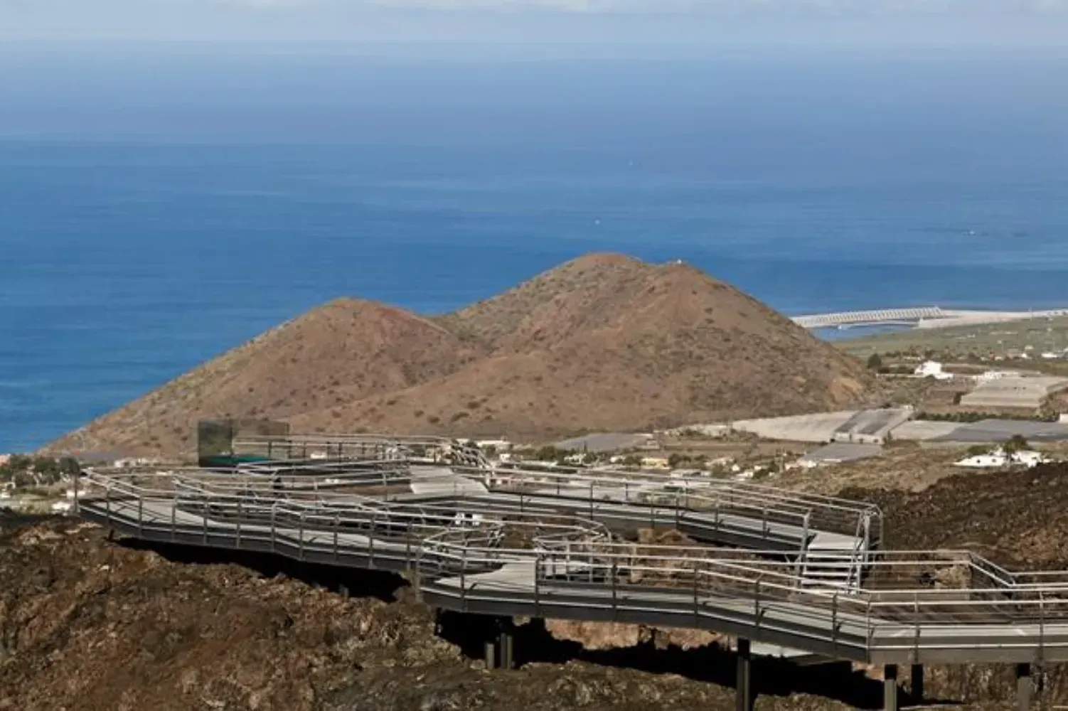 Hay un puente con vista al océano y las montañas.