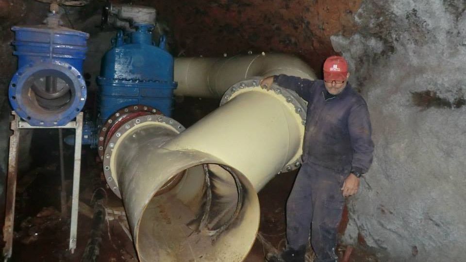 Un hombre está parado junto a una gran tubería en un túnel.