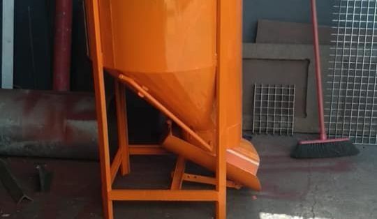 Un gran contenedor naranja se encuentra encima de un soporte de metal al lado de una escoba.