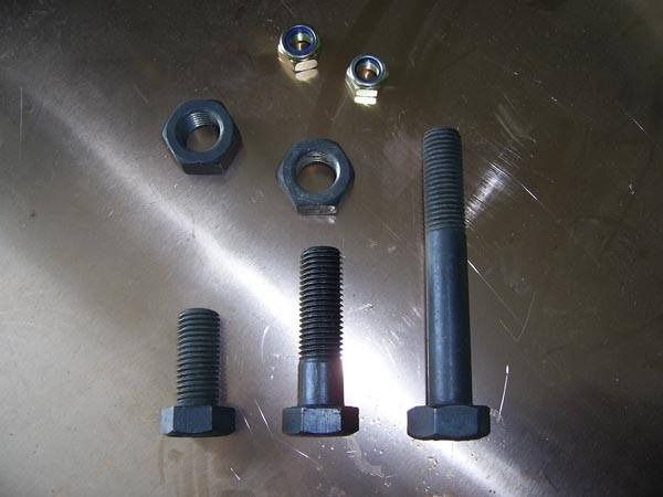 Tres tornillos y tuercas negros descansan sobre una superficie metálica.