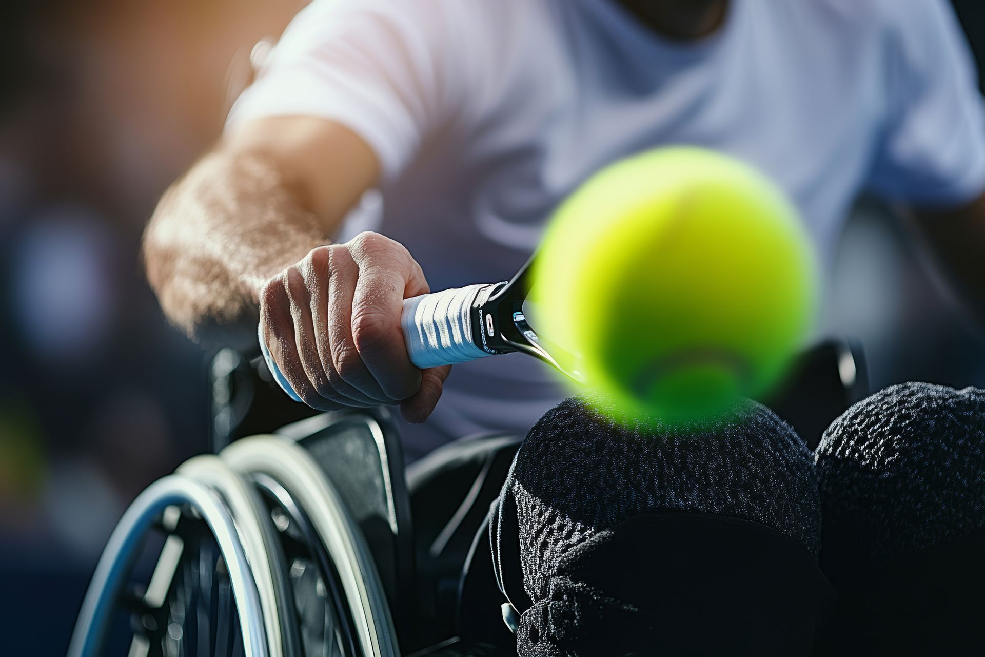 Persona en silla de ruedas jugando al tenis, golpeando una pelota amarilla con una raqueta.