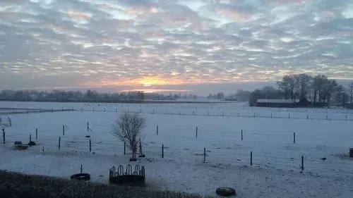ein verschneites Feld mit einem Zaun und einem Sonnenuntergang im Hintergrund.
