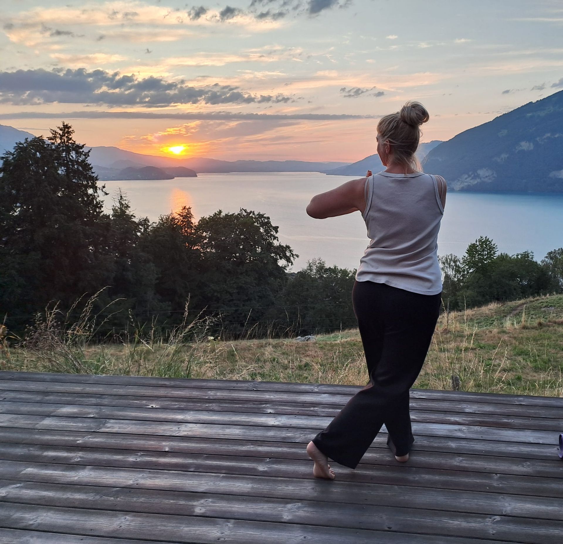 Eine Gruppe von Frauen macht an einem sonnigen Tag im Freien neben einem Pool Yoga, die Arme nach oben gewölbt.