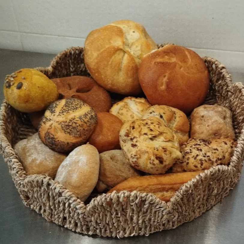 Cesta de panecillos variados, incluyendo pan de semillas de amapola, de cebolla y panes redondos crujientes.