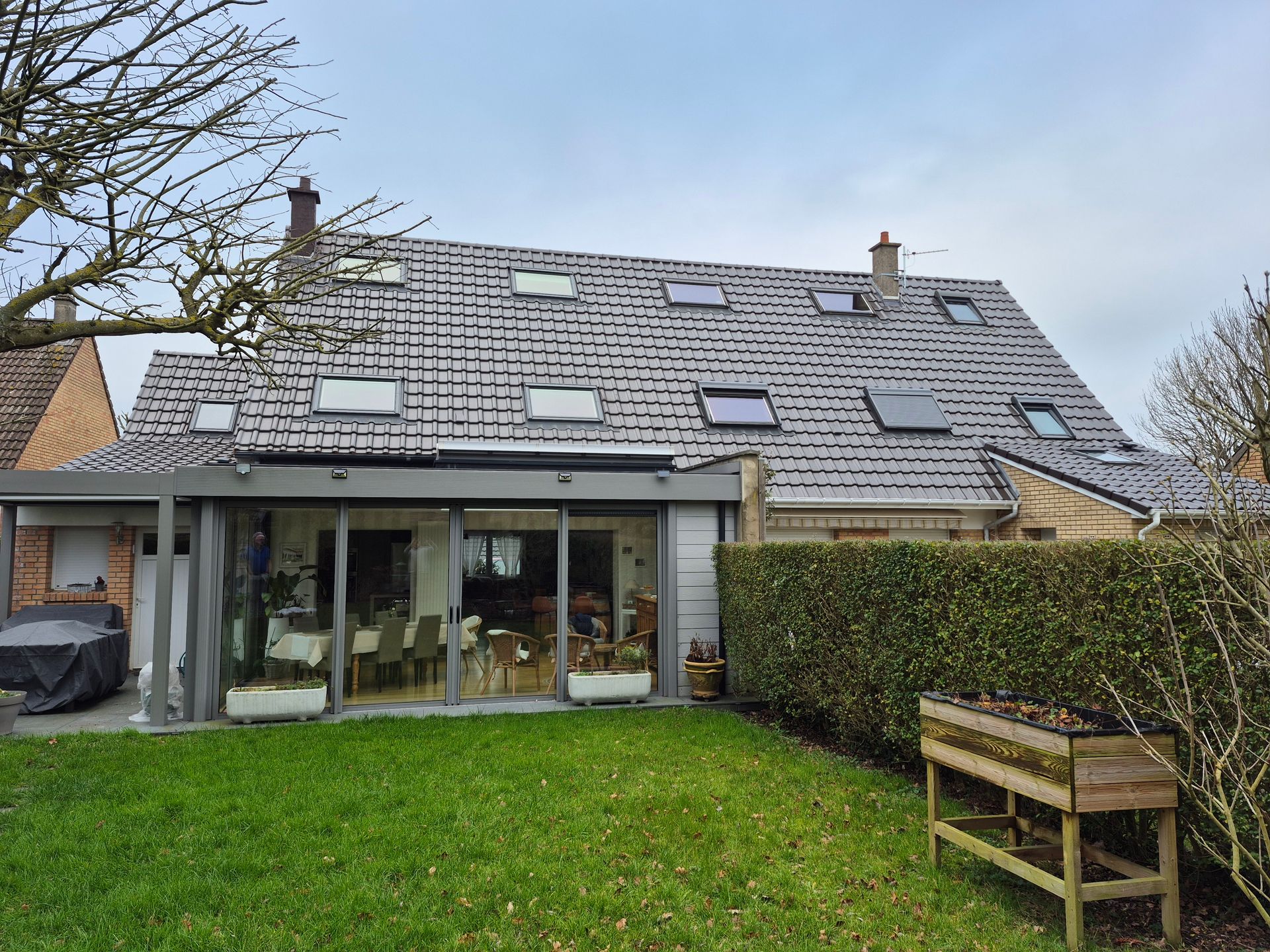 Une maison avec une extension aux parois de verre, un toit gris et une pelouse verte.