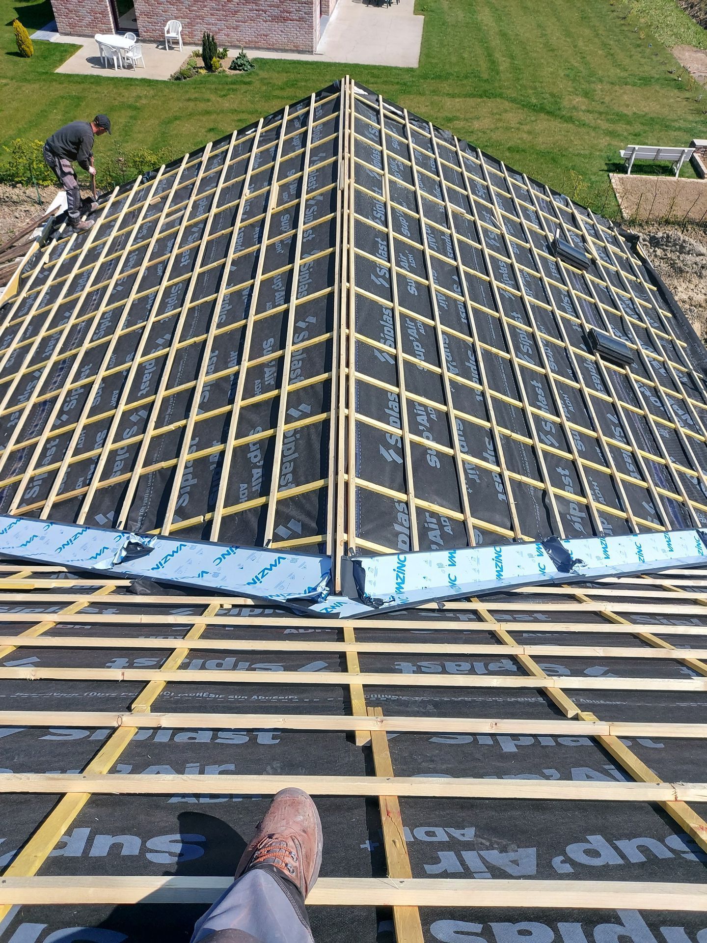 Construction de la toiture : sous-couche noire avec ossature en bois, ouvrier sur le toit.