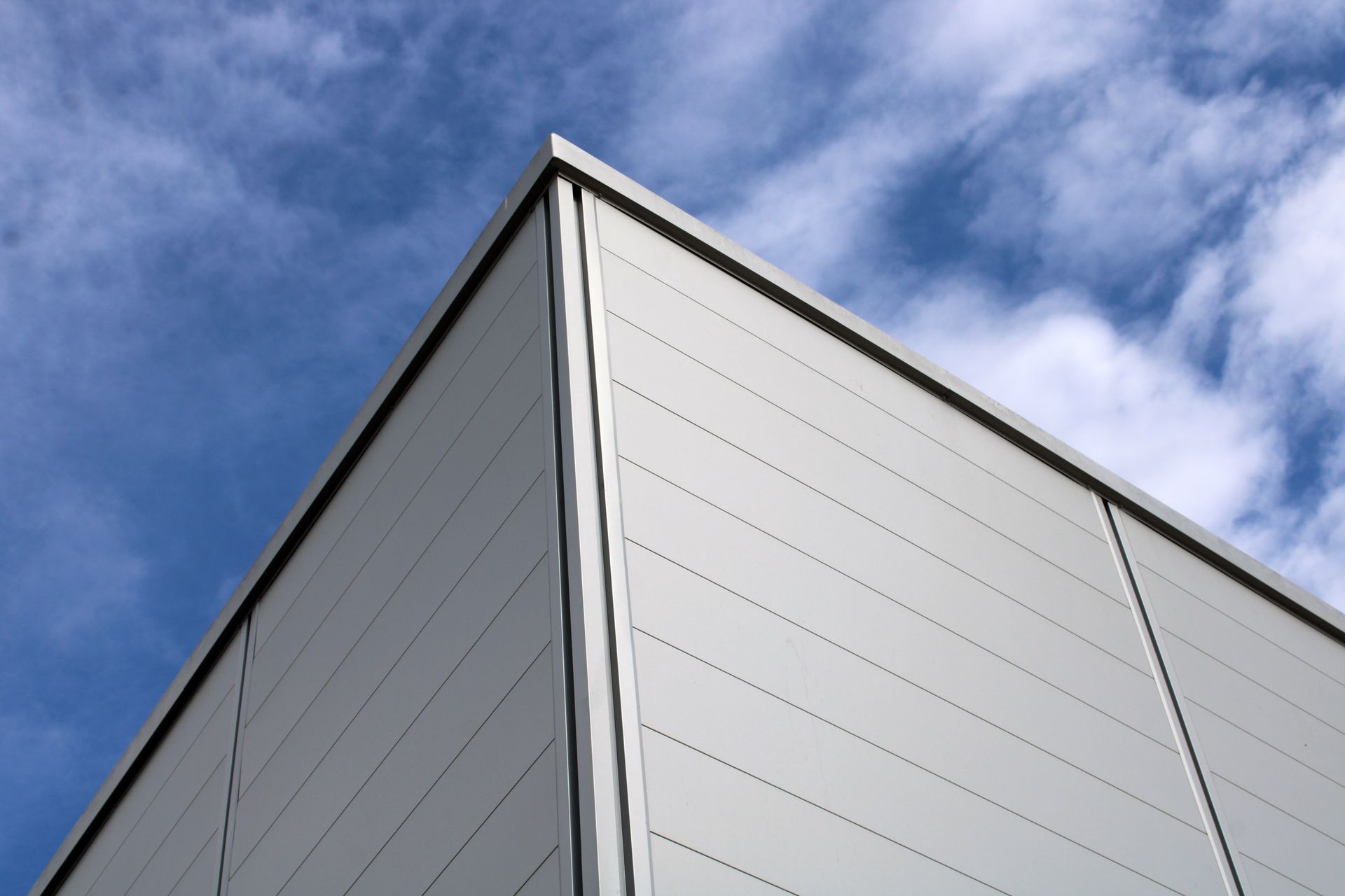 Coin d'un bâtiment moderne gris clair se détachant sur un ciel bleu parsemé de nuages ​​vaporeux.