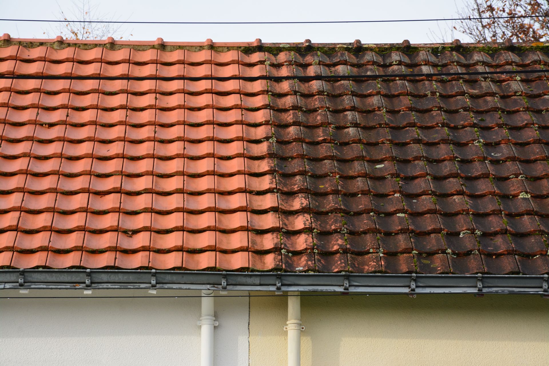 La moitié d'un toit de tuiles rouges nettoyée, l'autre moitié sale et sombre.