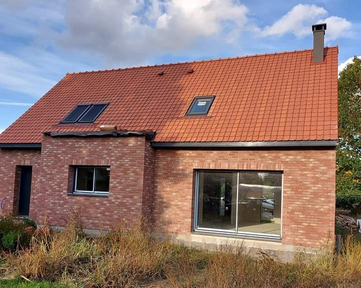 Maison en briques avec un toit de tuiles rouges et des panneaux solaires noirs.