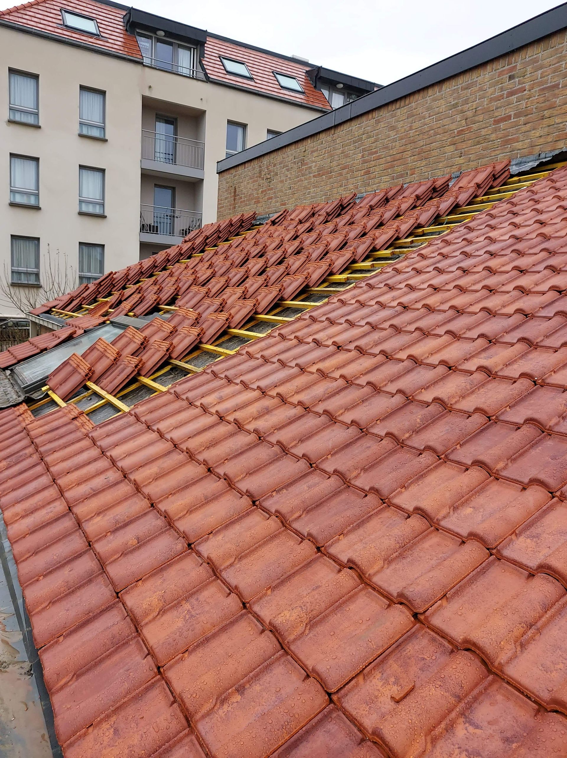 Toiture en tuiles rouges avec des échafaudages jaunes, bâtiment en arrière-plan.