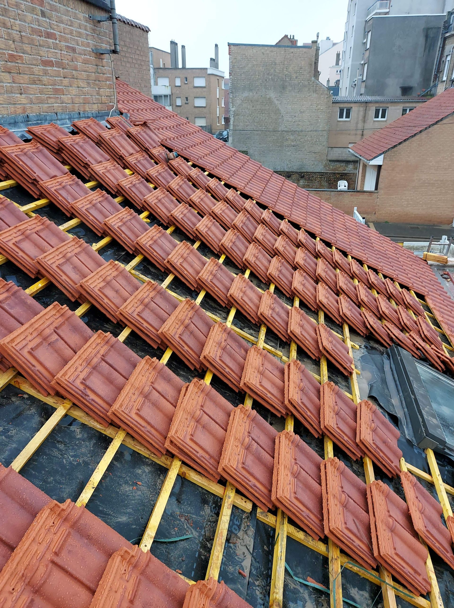 Tuiles rouges posées sur des supports en bois, chantier de construction en milieu urbain.