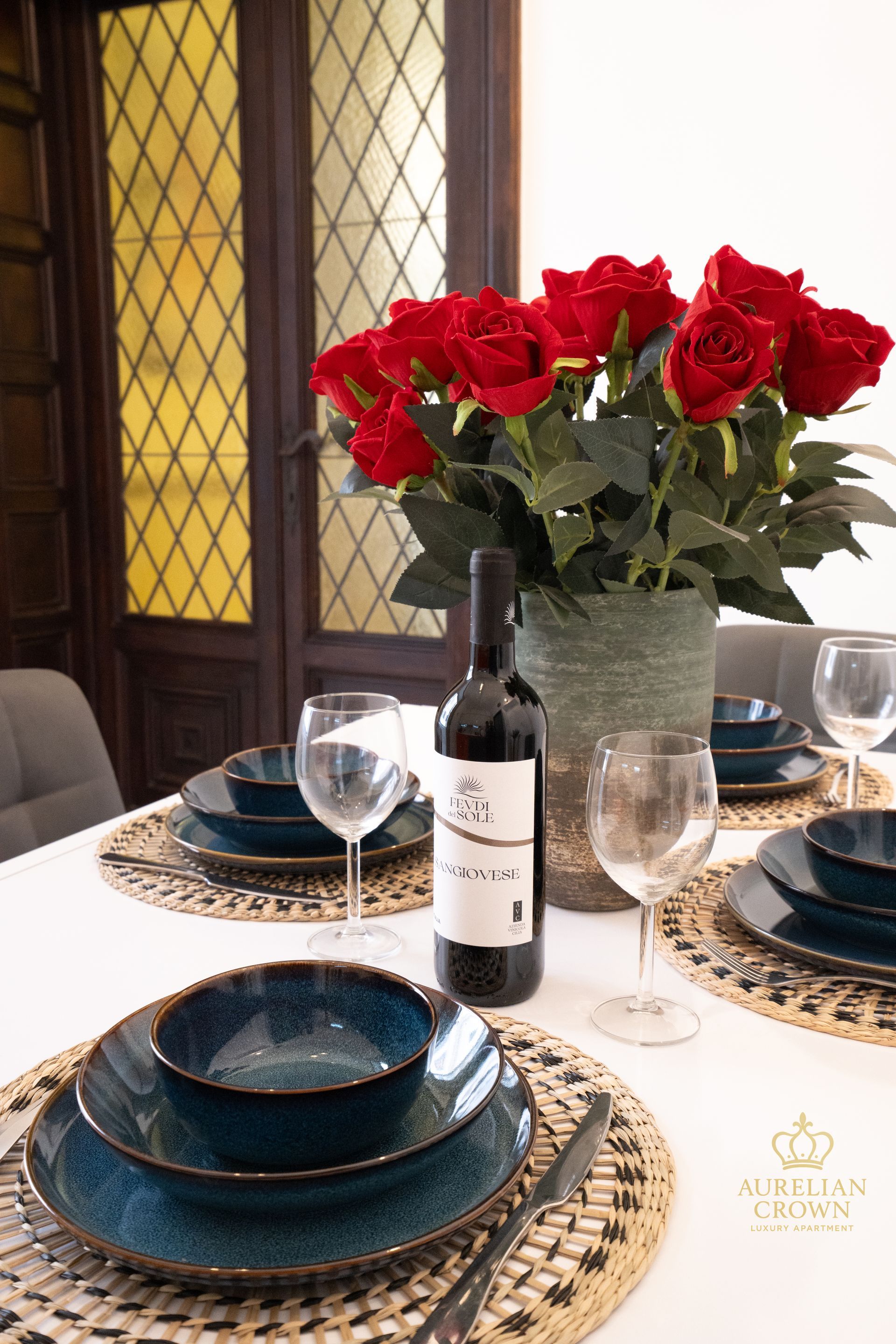 Dining table set with blue plates, wine, roses, and place settings.