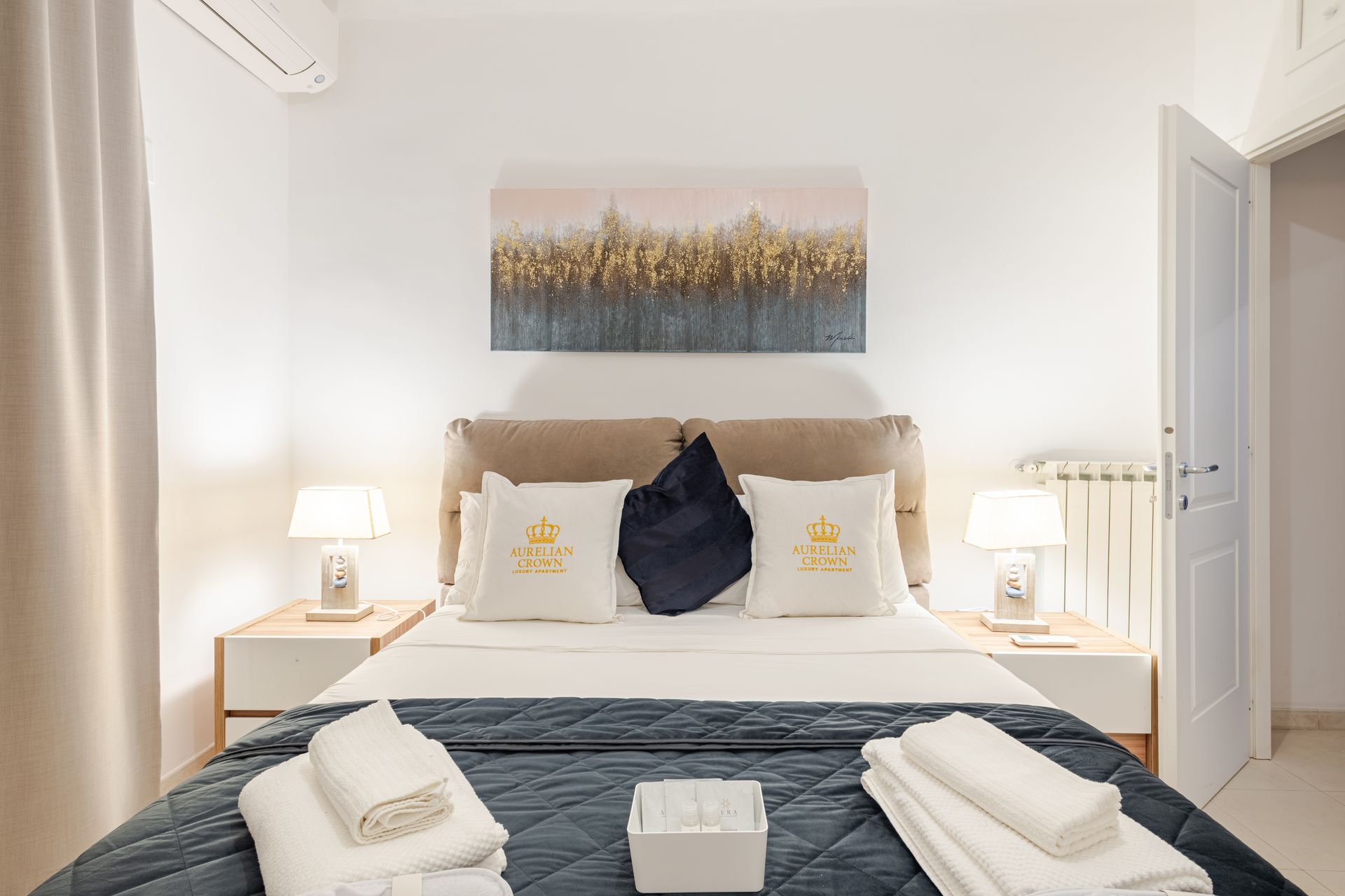 Bedroom with a double bed, white walls, nightstands, lamps, and artwork.