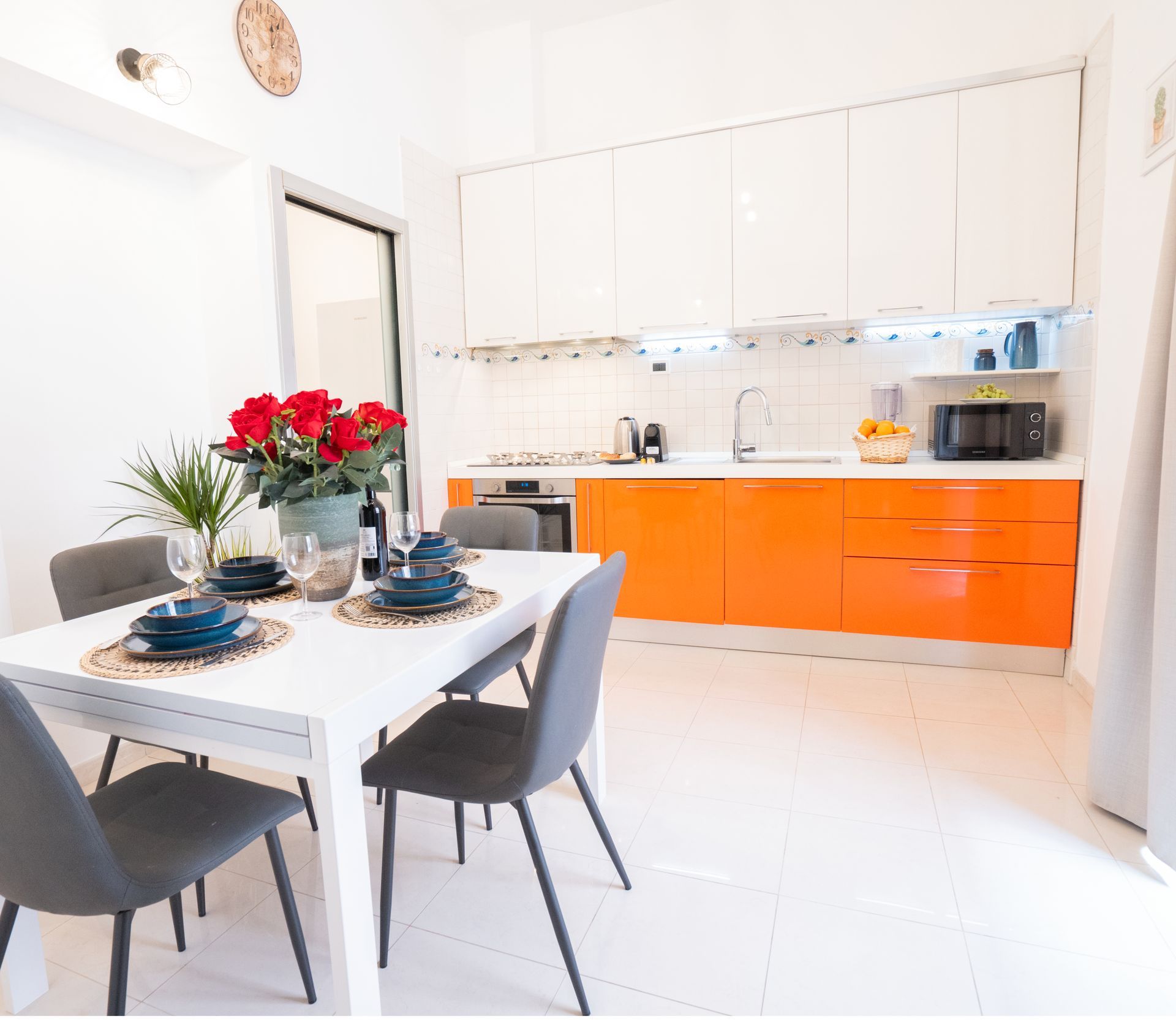 Modern kitchen and dining area with white cabinets and orange accents; dining table set for a meal.