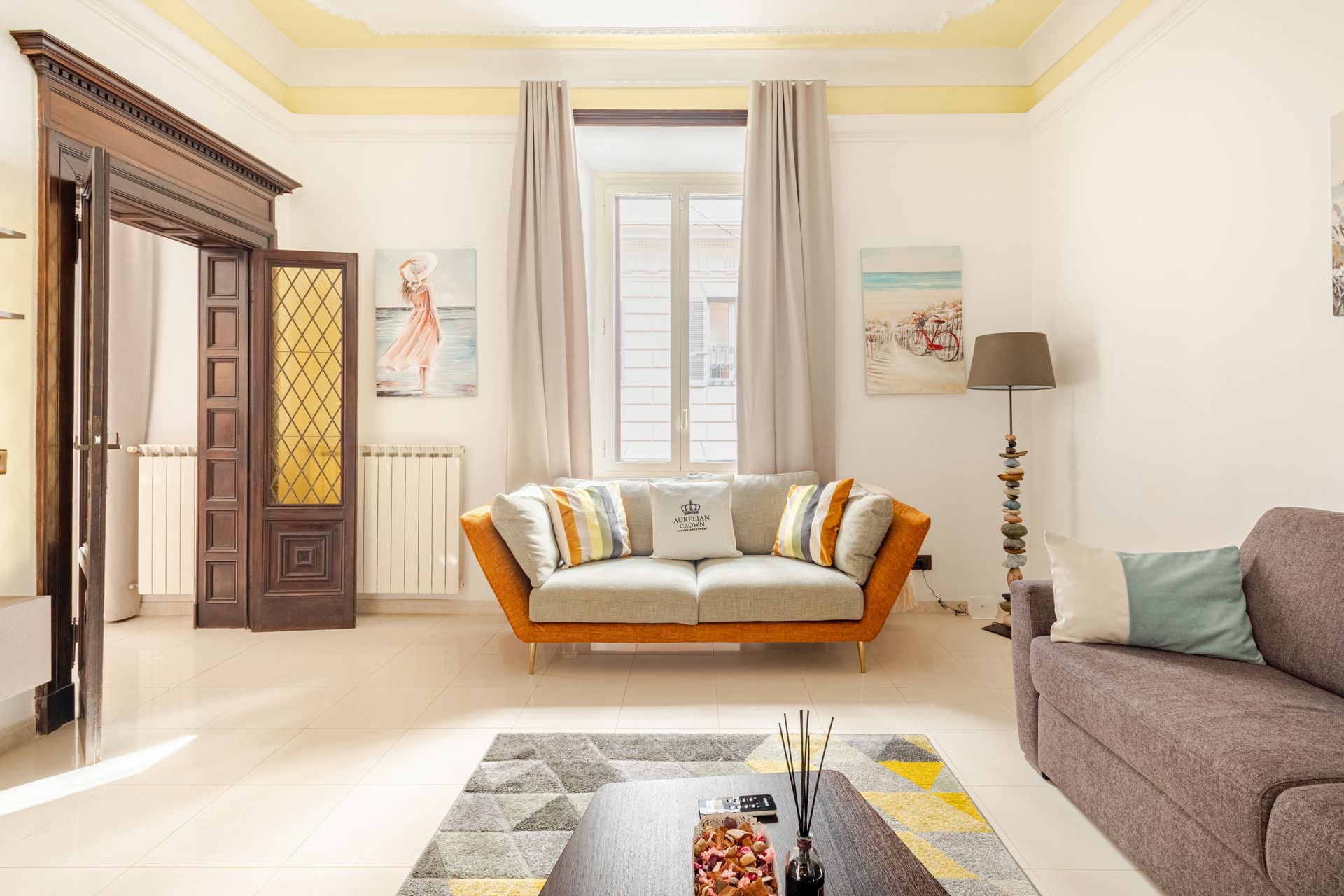 Living room with orange and gray sofas, window, paintings, and a decorative doorway.