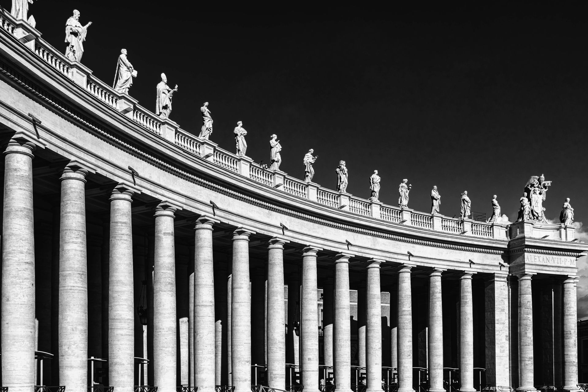 Colonnade of St. Peter's Square, Vatican City, with statues atop columns under a bright sky.