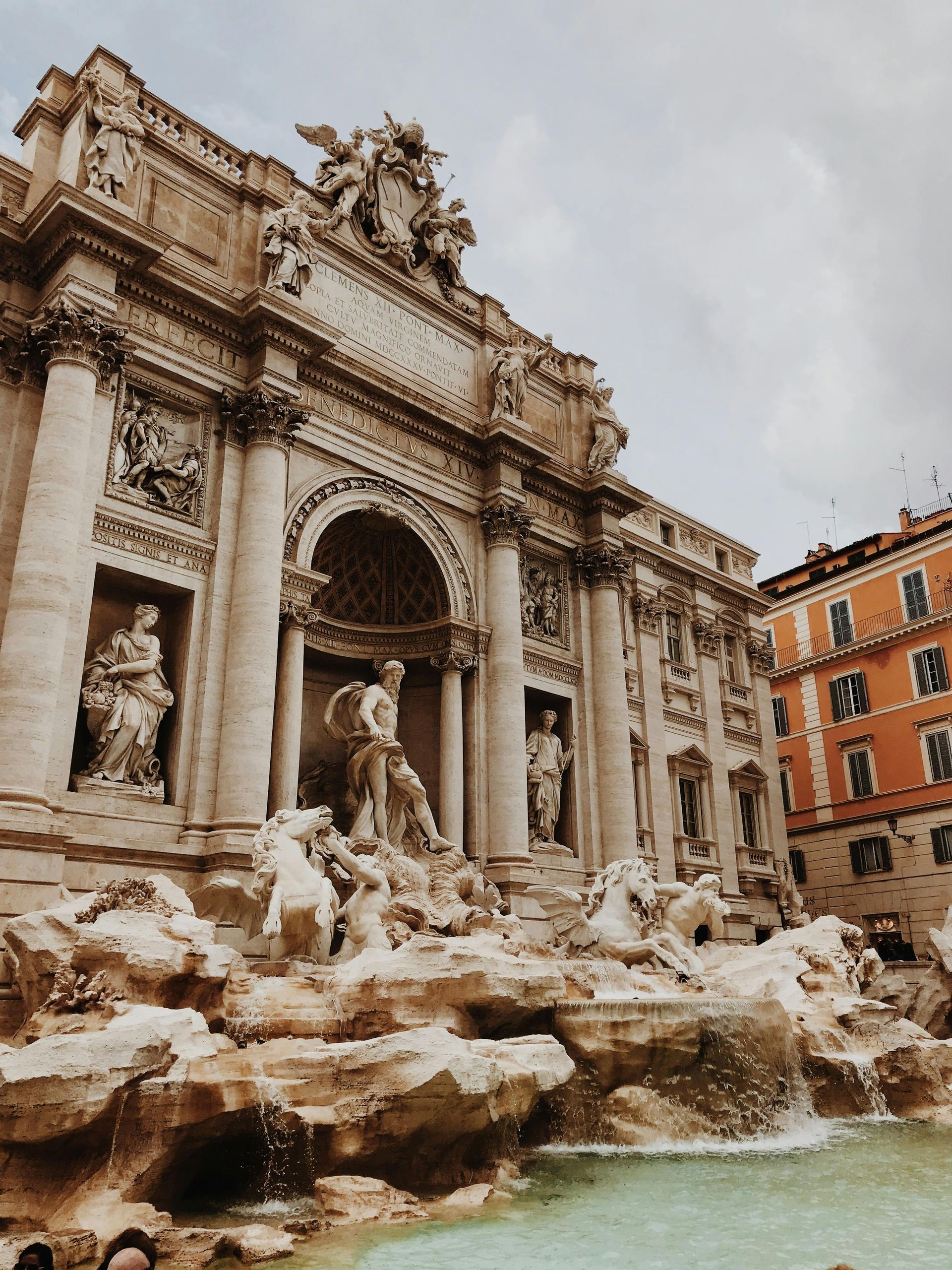 Trevi Fountain in Rome, Italy. Baroque architecture with sculptures, water cascading into a turquoise pool, and overcast sky.