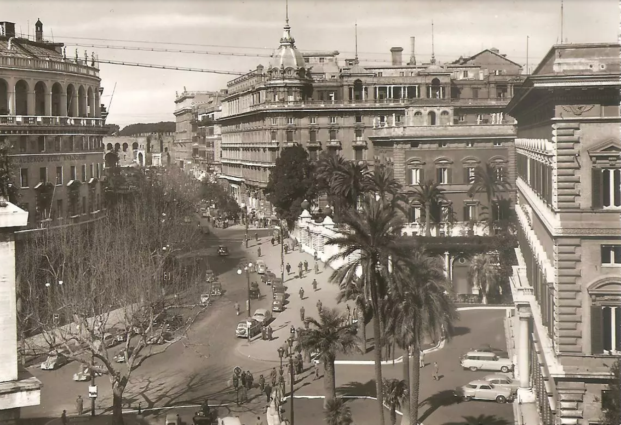 Vintage street scene with cars, palm trees, and multi-story buildings.