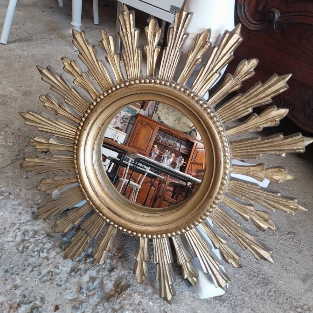 Miroir doré en forme de soleil reflétant un magasin d'antiquités encombré.