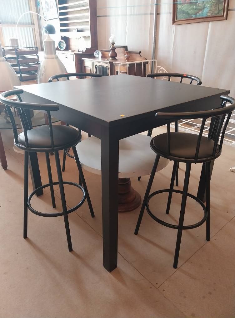 Table carrée foncée avec quatre tabourets de bar noirs.