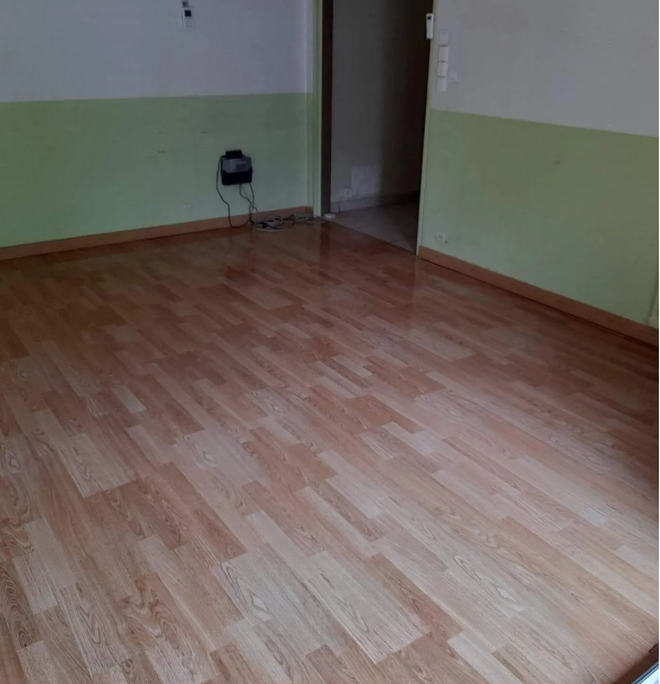 Pièce vide avec sol stratifié marron clair, murs vert clair et blancs et une porte.