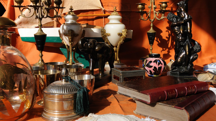 Des objets anciens exposés sur une table, notamment des vases, des chandeliers, des livres et une statue.