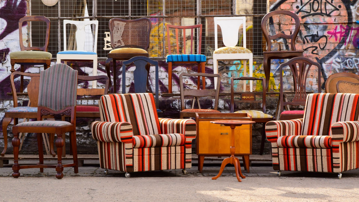 Chaises vintage assorties et deux fauteuils rayés contre un mur couvert de graffitis.