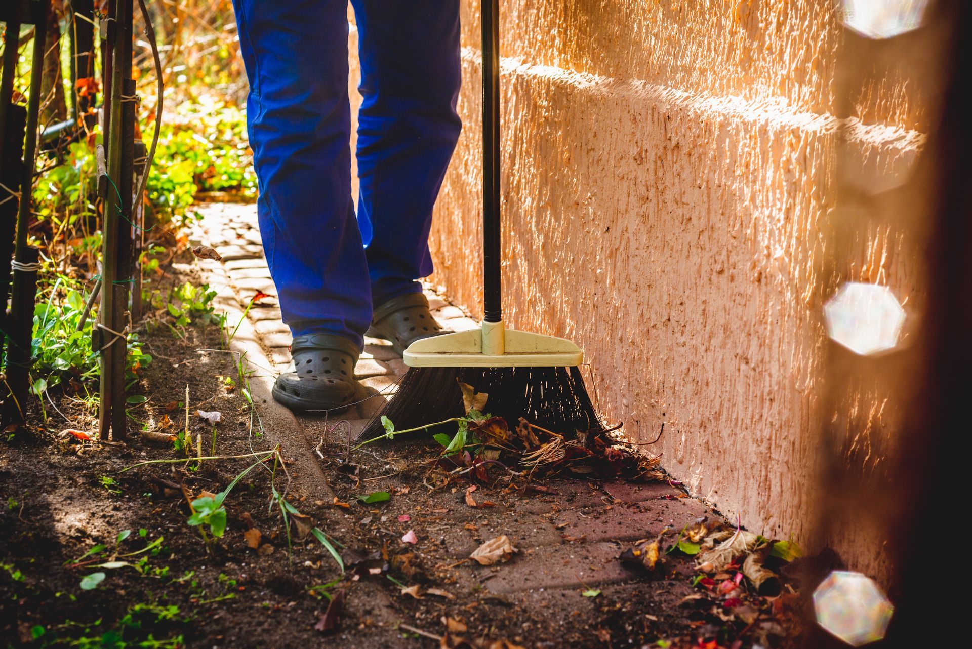 Une personne en pantalon bleu balaye des débris près d'un mur en extérieur.