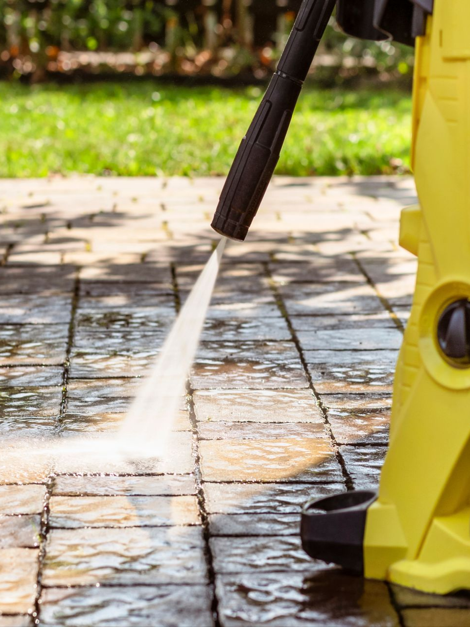 Nettoyeur à haute pression jaune pulvérisant de l'eau sur un patio en briques.