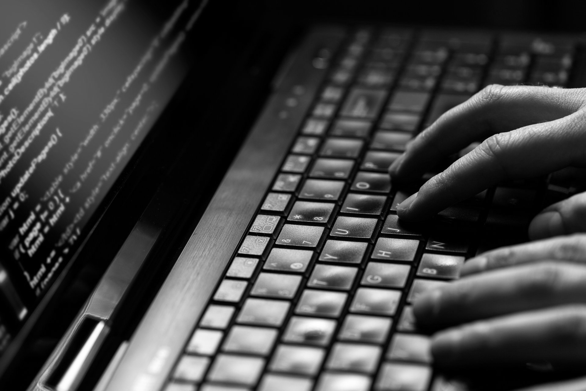 Des mains tapant sur un clavier d'ordinateur affichant du code en noir et blanc.