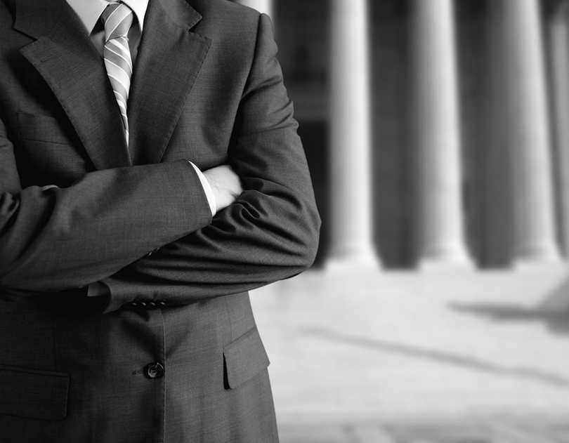 Portrait en noir et blanc d'une personne en costume, les bras croisés, devant des colonnes